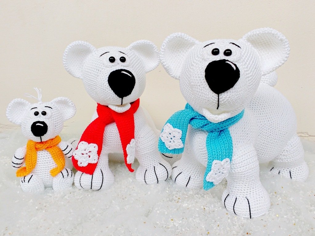 Drei gehäkelte weiße Eisbären in verschiedenen Größen, jeder trägt einen bunten Schal mit Schneeflocken-Applikation.