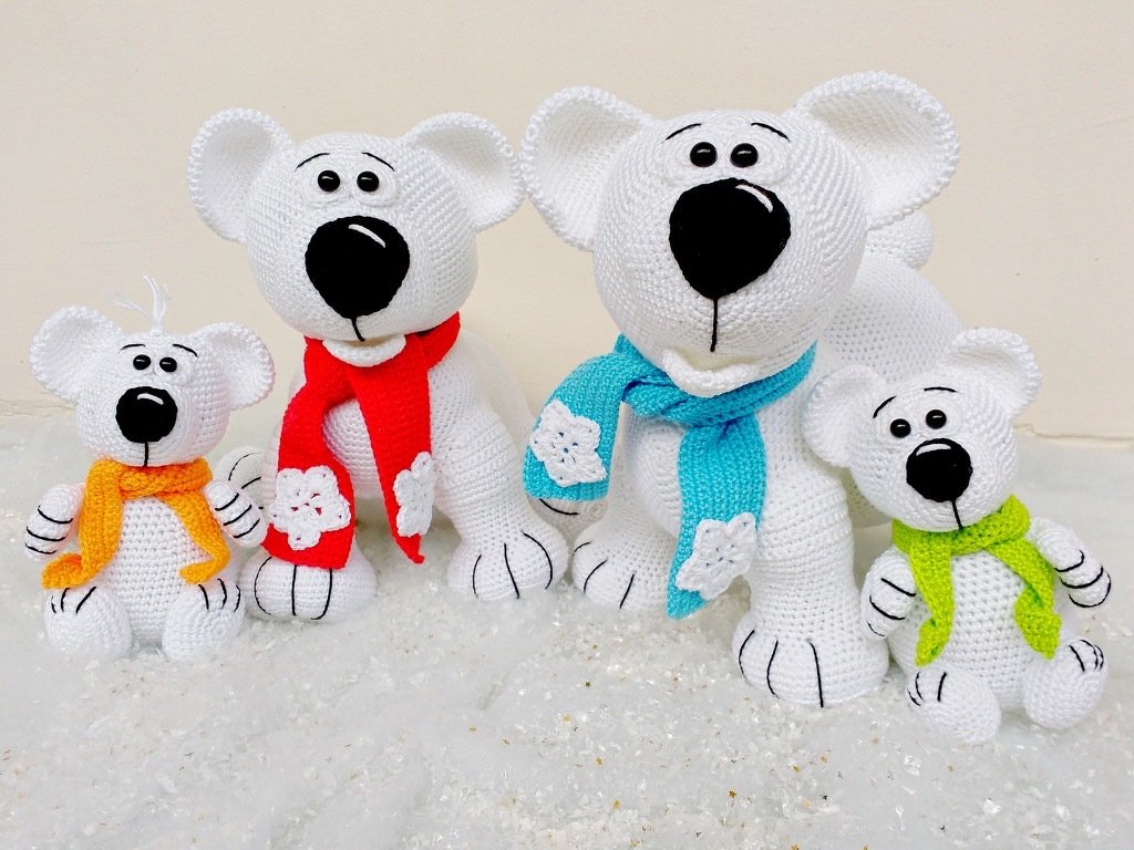 Four white crocheted amigurumi bears with black noses and colorful scarves on a snow-like background