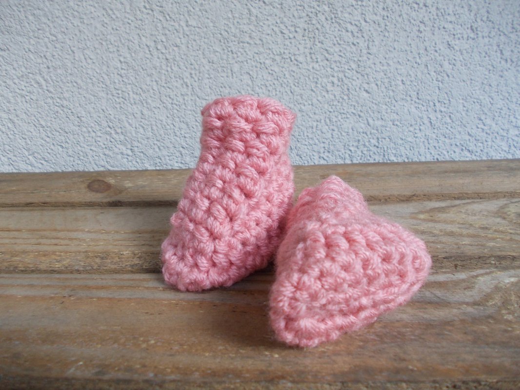 paar rosa Baby-Booties aus grober Masche auf Holzbrett