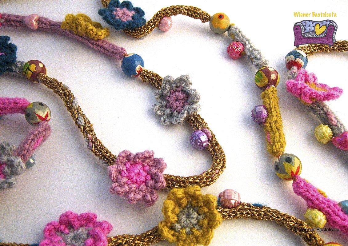 Bunte gehäkelte Kette mit kleinen Häkelblüten, farbigen Perlen und goldfarbenem Zopf.