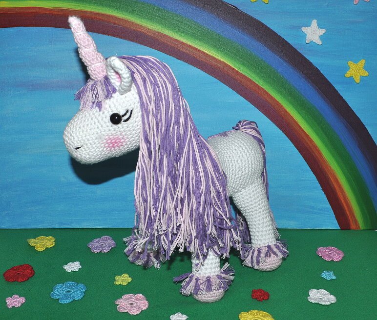 Detaillierte Ansicht eines gehäkelten Einhorn-Amigurumi mit lila-weißer Mähne, spiralförmigem Horn und fransigen Hufen