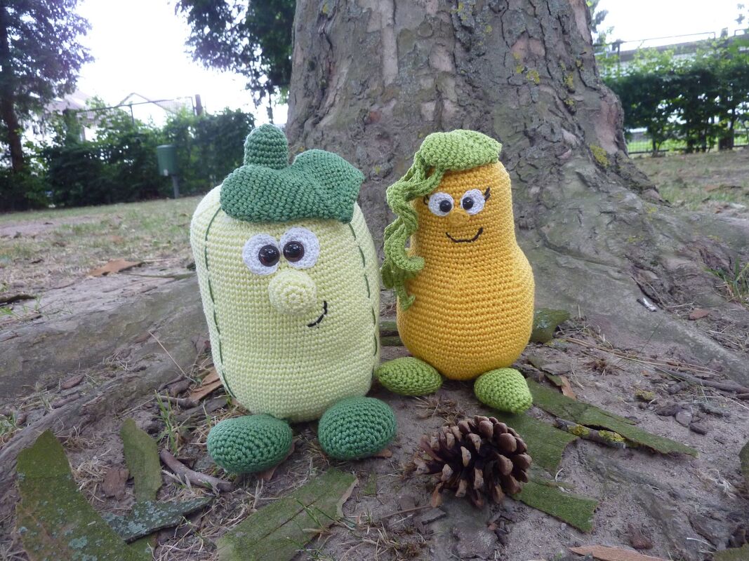 Zwei fröhliche, kürbisähnliche gehäkelte Figuren mit Gesicht vor Baumstamm