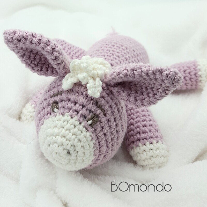 Gehäkeltes lila Amigurumi‑Eselchen mit weißen Details auf weißem Stoff