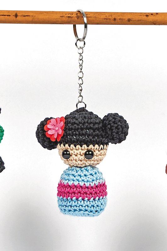 Gehäkelter Amigurumi-Schlüsselanhänger mit schwarzem Dutt, rosa Blume und blau-pink gestreiftem Körper