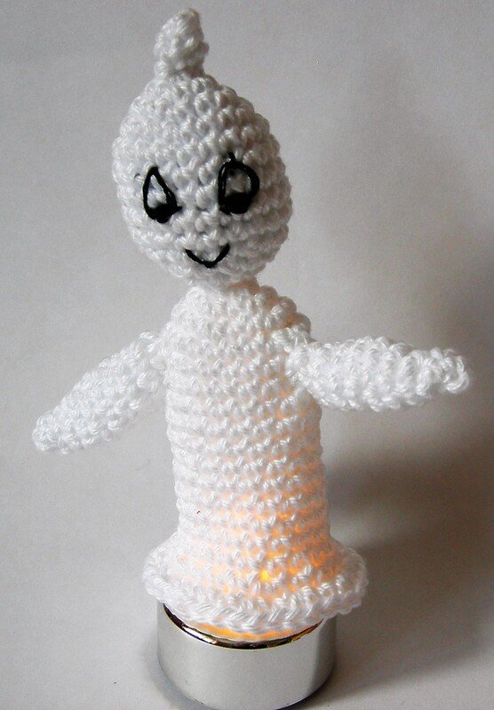Gehäkelter weißer Amigurumi-Geist mit aufgesticktem Gesicht, beleuchtet von einem Teelicht.