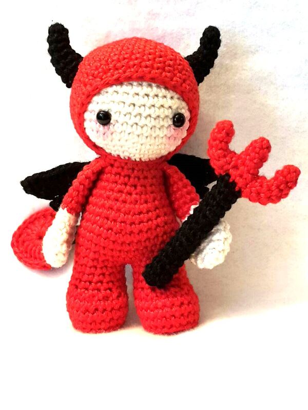 Rotes gehäkeltes Amigurumi-Teufelchen mit weißem Gesicht, schwarzen Hörnern, Flügeln und Dreizack