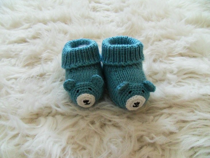 Zwei türkise Baby-Bärenschuhe, gehäkelt, auf flauschigem weißen Hintergrund