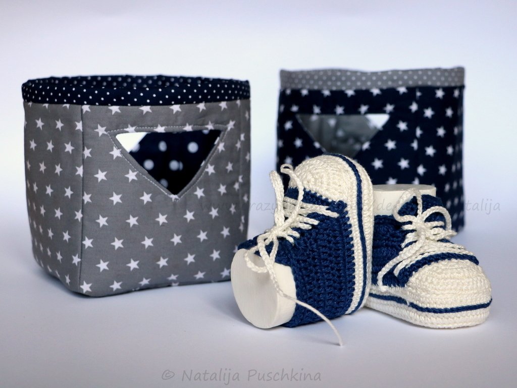 Maritime gehäkelte Babysneaker in Blau und Creme neben zwei Stoffkörben mit Sternenmuster