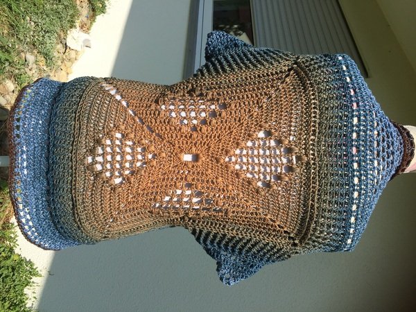 Gehäkelter Seelenwärmer in Braun und Blau mit zentralem Lochmuster, auf Schaufensterpuppe im Freien.