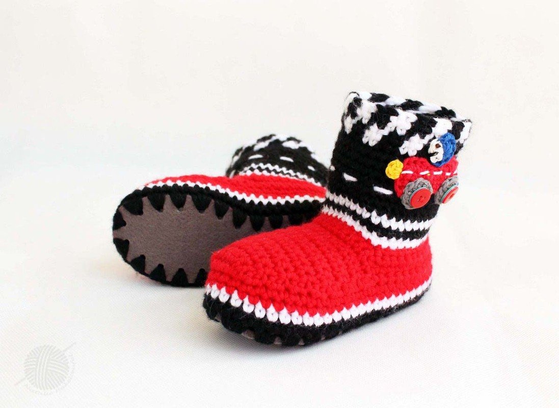 Ein Paar gehäkelter Babystiefel in Rot, Schwarz und Weiß mit Rennwagen-Applikation und Schachbrettmuster am Schaft.