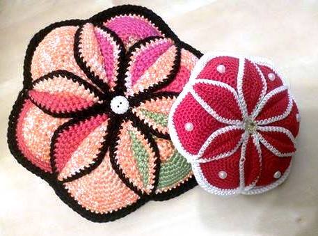 Rundes gehäkeltes Blumenkissen neben gehäkeltem blütenförmigem Deckchen