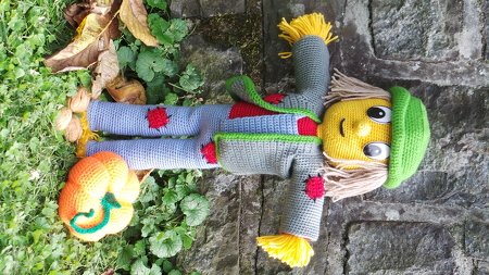 Amigurumi-Vogelscheuche mit grüner Mütze, grauem Mantel und kleinem gehäkelten Kürbis