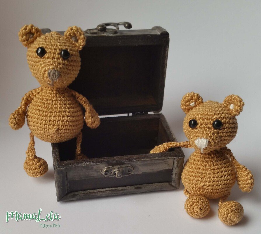 Zwei kleine gehäkelte Teddys aus gelbem Garn neben offener Holztruhe