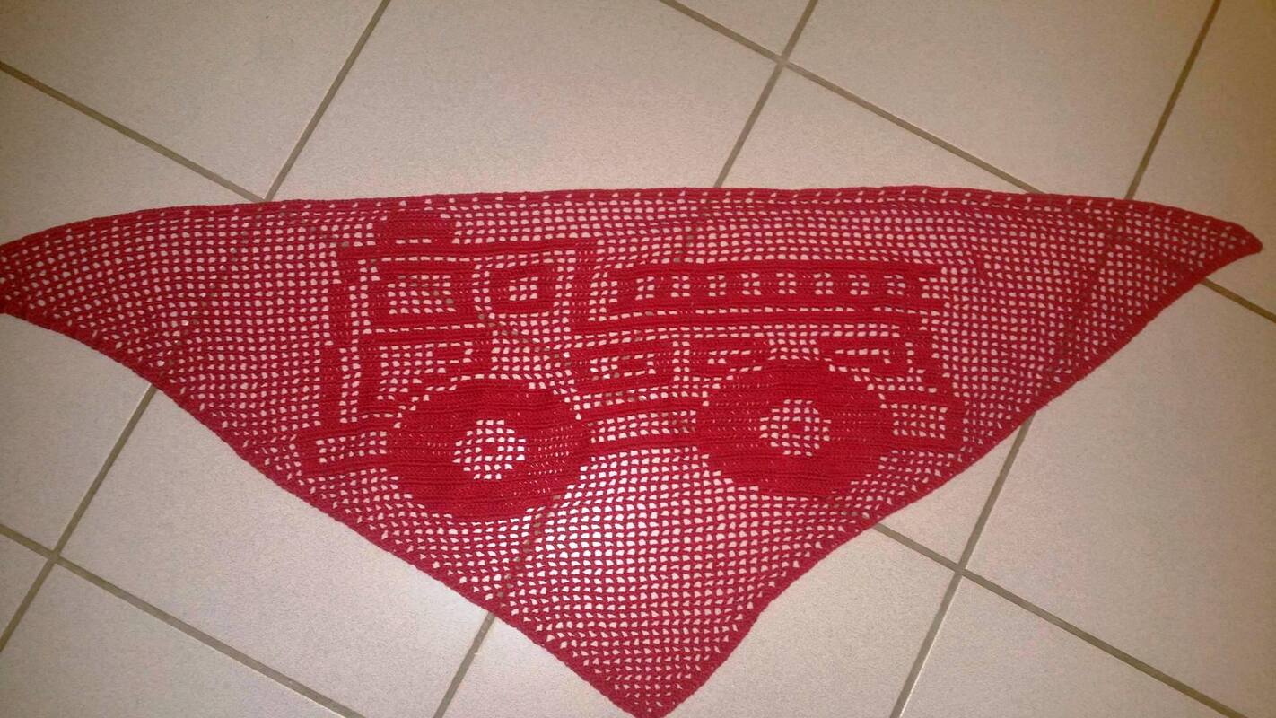 Rotes, dreieckiges, gehäkeltes Tuch mit Feuerwehrauto‑Motiv auf hellem Fliesenboden.