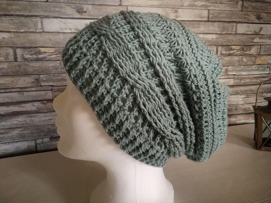 Schaufensterkopf mit gehäkelter salbeigrüner Slouch-Mütze mit Zopf- und Rippenmuster