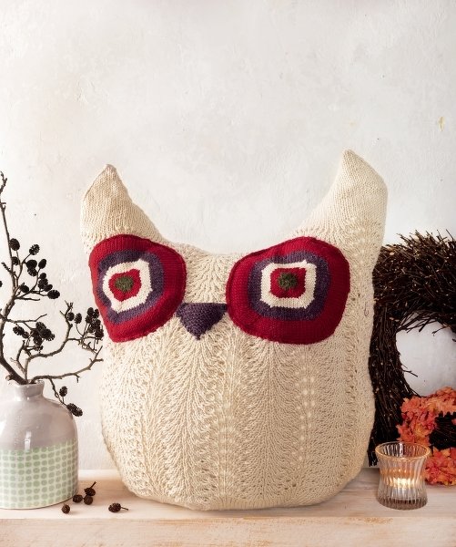 Cremefarbenes gestricktes Eulenkissen mit roten und violetten Augen auf einem Regal