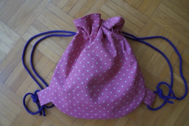 kleiner rosa Kordelbeutel mit weißen Punkten und violetten Tragekordeln