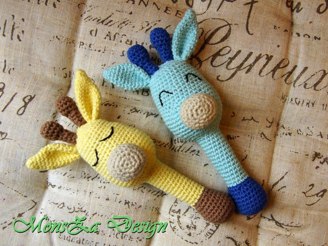 Zwei gehäkelte Giraffenrasseln in Gelb und Türkis auf einem gemusterten Stoffhintergrund.