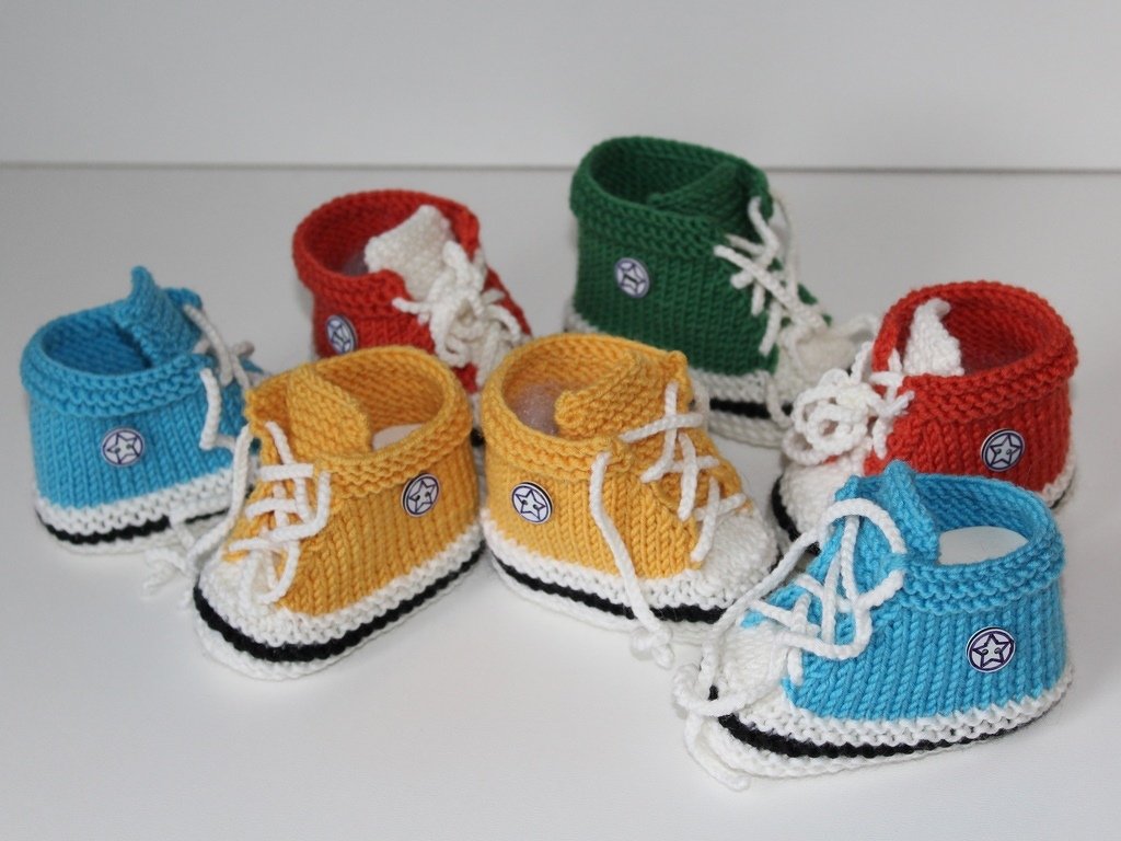 Mehrere gestrickte Babyschuhe im Sneaker-Stil in Blau, Gelb, Rot und Grün mit weißen Schnürsenkeln