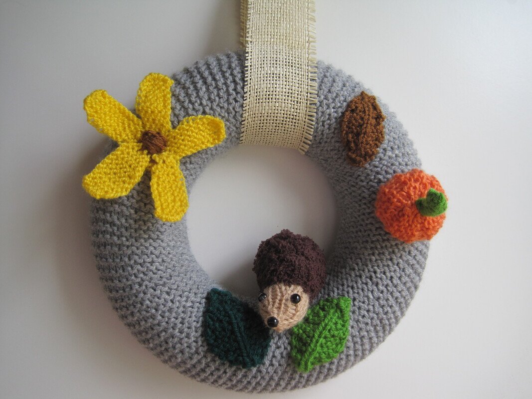 Gestrickter grauer Kranz mit Igel-, Kürbis- und Blumenapplikationen an hellem Band