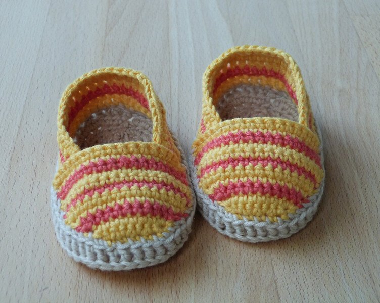 Paar gehäkelter Babyschuhe gelb-rosa mit beigem Rand auf Holzuntergrund