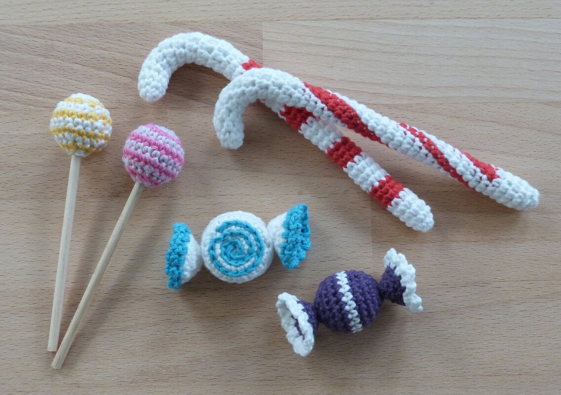 Nahaufnahme gehäkelter Zuckerstangen, Lutscher und Bonbons in verschiedenen Farben auf einem Holztisch.