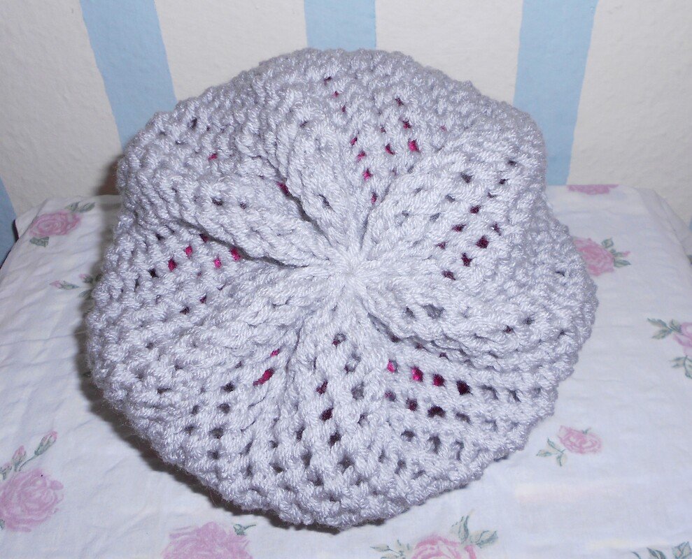 Hellgraue Strickmütze mit Lochmuster und fuchsiafarbenem Innenfutter auf gemustertem Stoff