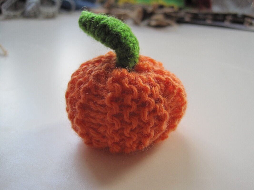 Gestrickter orangefarbener Zierkürbis mit grünem Stiel auf hellem Untergrund