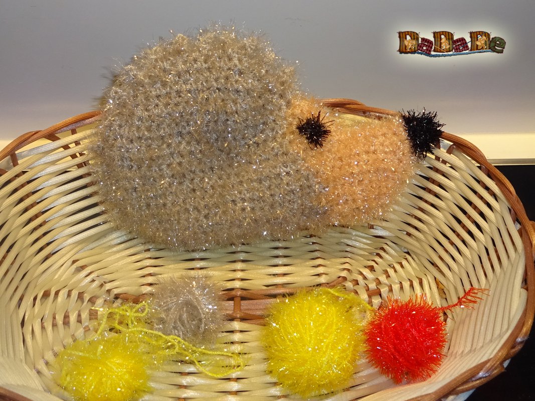 Gehäkelter Igel aus goldbraunem Effektgarn im Weidenkorb mit gelben und roten Pompons
