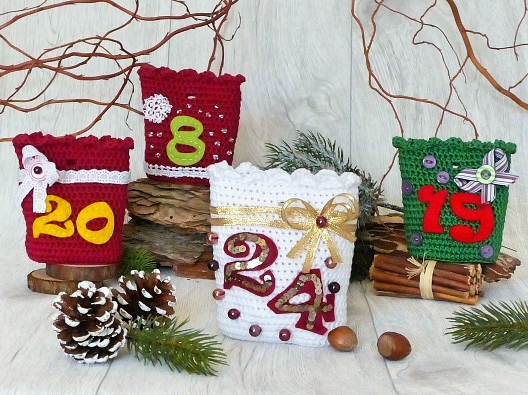 Gehäkelte Advents‑Taschen in Rot, Weiß und Grün mit Filz‑Zahlen, Perlen und Schleifen, dekorativ arrangiert mit Tannenzweigen und Zapfen