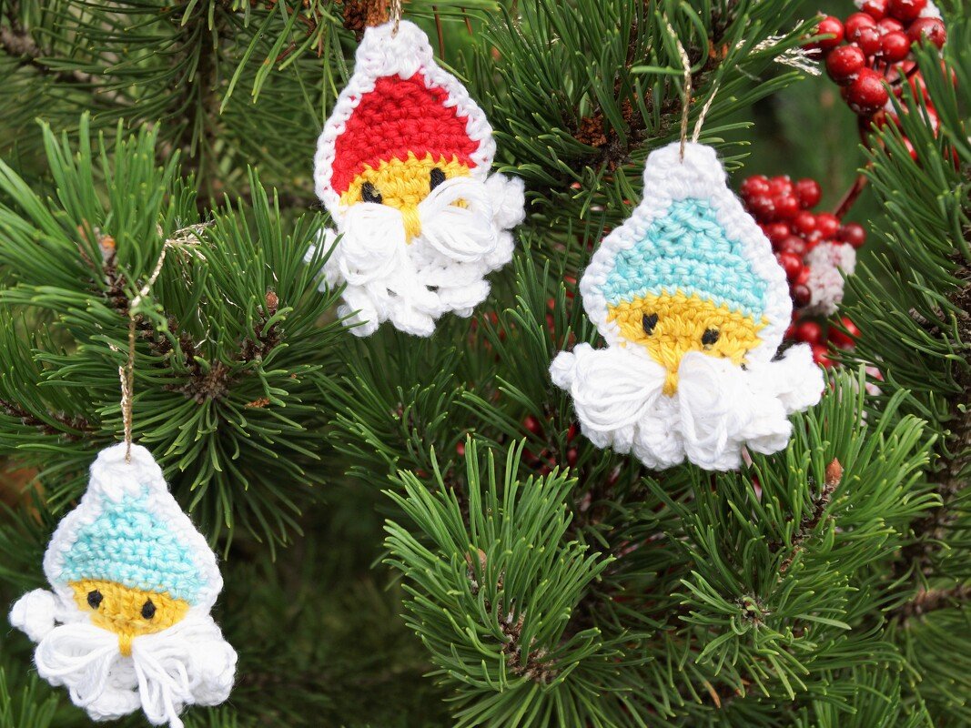 Drei gehäkelte Wichtel-Anhänger mit roter und hellblauen Mützen an einem Kiefernzweig