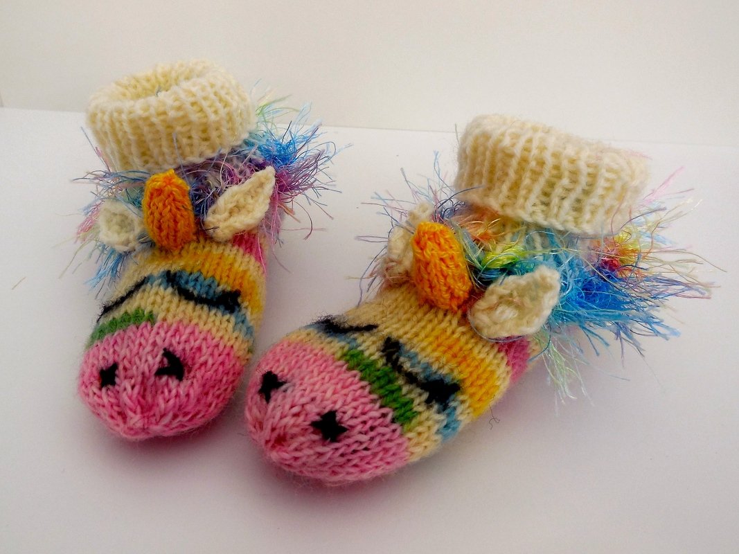 Paar handgestrickter Einhorn-Babyschuhe in Regenbogenfarben auf hellem Hintergrund