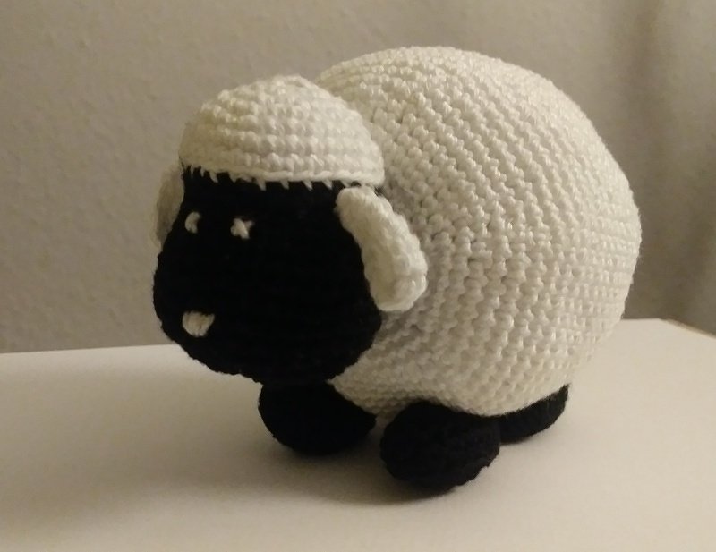Gehäkeltes Amigurumi-Schaf mit rundem weißen Körper und schwarzem Gesicht und Pfoten