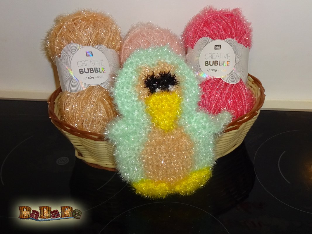 Kompaktes gehäkeltes Entchen in Mint, Gelb und Beige vor Korb mit Effektgarn