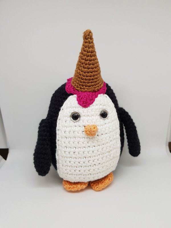 Gehäkelter Amigurumi-Pinguin, weißer Bauch, schwarze Flügel, orangefarbener Schnabel und Füße, braunes Horn mit pinker Basis