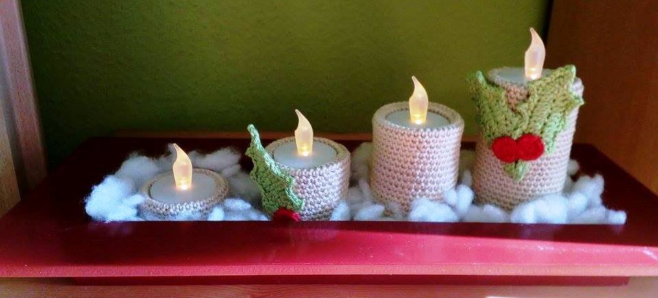 Vier LED-Teelichter in gehäkelten Hüllen, zwei mit grünen Blättern und roten Beeren, auf rotem Tablett mit Kunstschnee