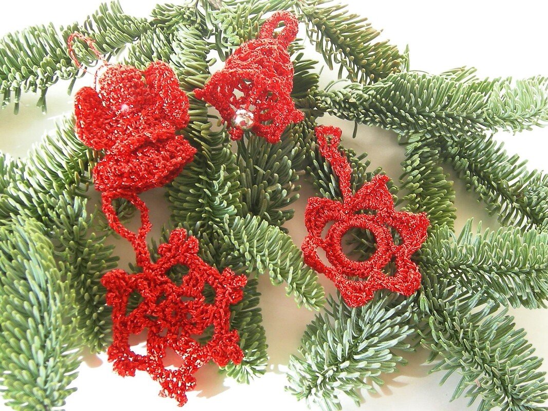 Rote gehäkelte Weihnachtsanhänger (Engel, Glocke, Stern, Schneeflocke) auf Tannenzweigen.
