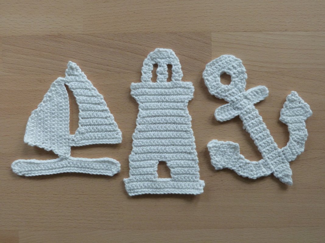 Weiße gehäkelte Applikationen: Segelboot, Leuchtturm und Anker auf Holzuntergrund