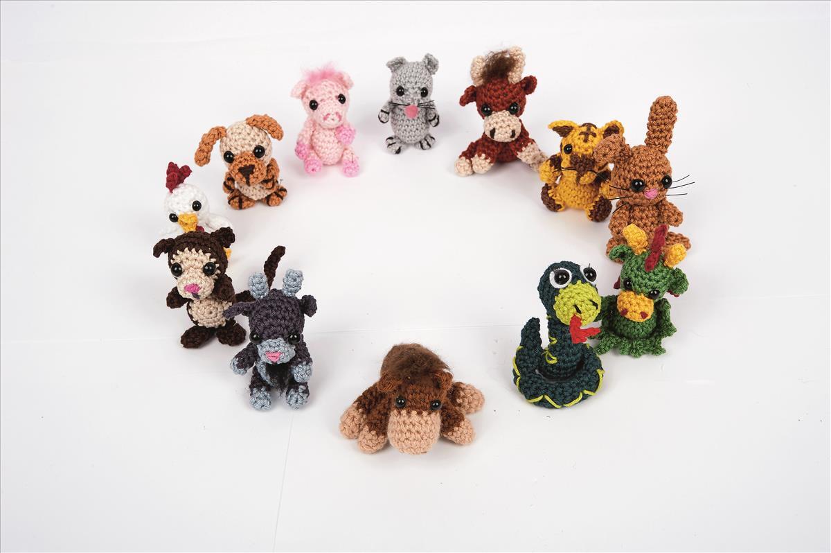Zwölf gehäkelte Amigurumi-Tiere — darunter Schwein, Maus, Ochse, Tiger, Hase, Drache, Schlange, Pferd, Ziege, Affe, Hahn und Hund — angeordnet in einem Kreis auf weißem Grund.