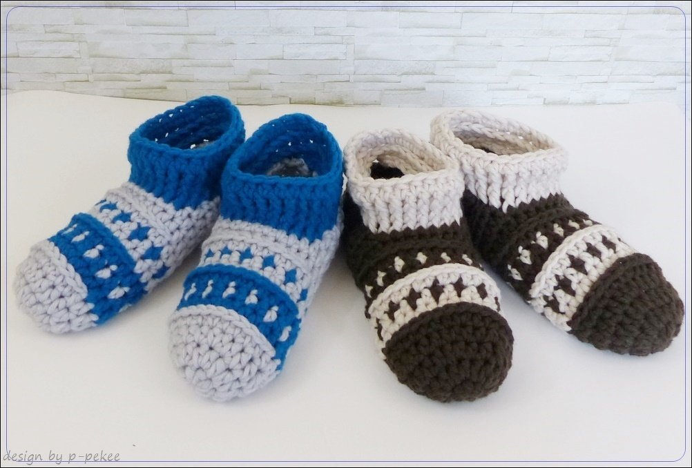 Zwei Paar gehäkelte Kinderschuhe in Blau/Grau und Braun/Beige nebeneinander auf hellem Untergrund