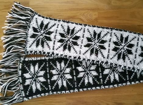 Gestrickter schwarz
weißer Schal mit wiederholtem Sternmuster und Fransen, beide Farbausführungen sichtbar