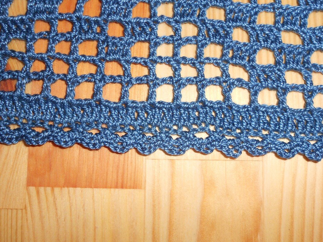 Blaues gehäkeltes Netzmuster mit wellenförmigem Muschelsaum auf Holz