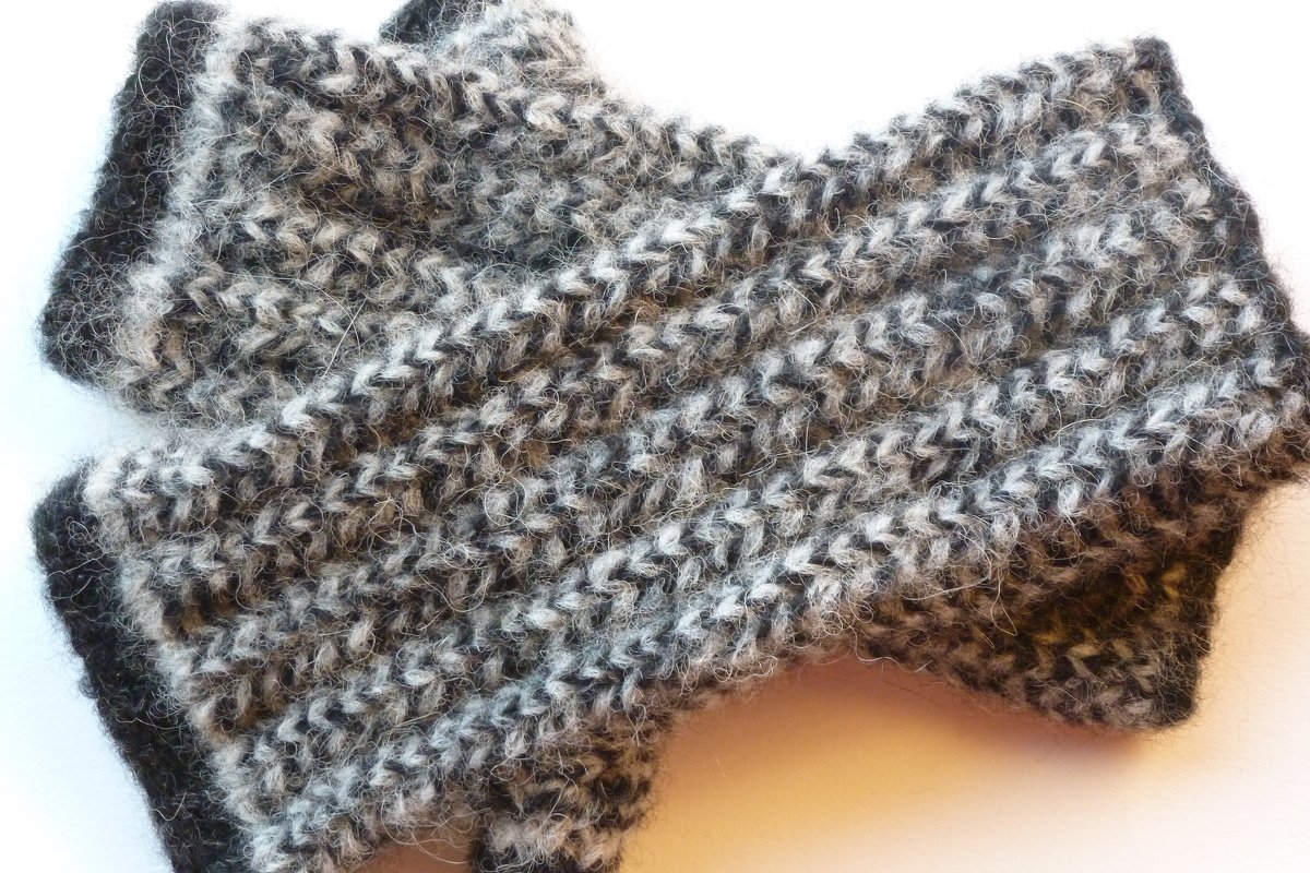 Nahaufnahme melierter gestrickter Armstulpen in Schwarz und Weiß mit sichtbarem V-förmigem Maschenbild und flauschiger Oberfläche.