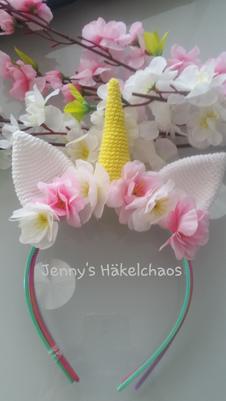 Gehäkeltes Einhorn-Stirnband mit gelbem Horn, weißen Ohren und rosa Blüten auf mehrfarbigem Haarreif