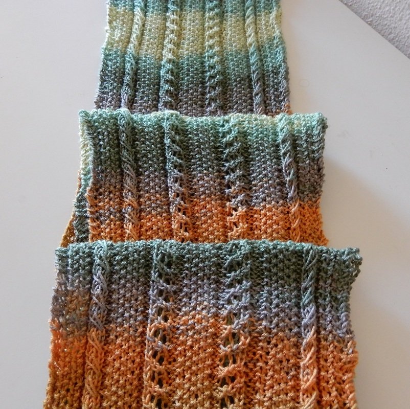 Nahaufnahme eines mehrfarbigen gestrickten Schals mit Farbverlauf und Rippen- sowie Lochmuster in Grün, Orange und Beige