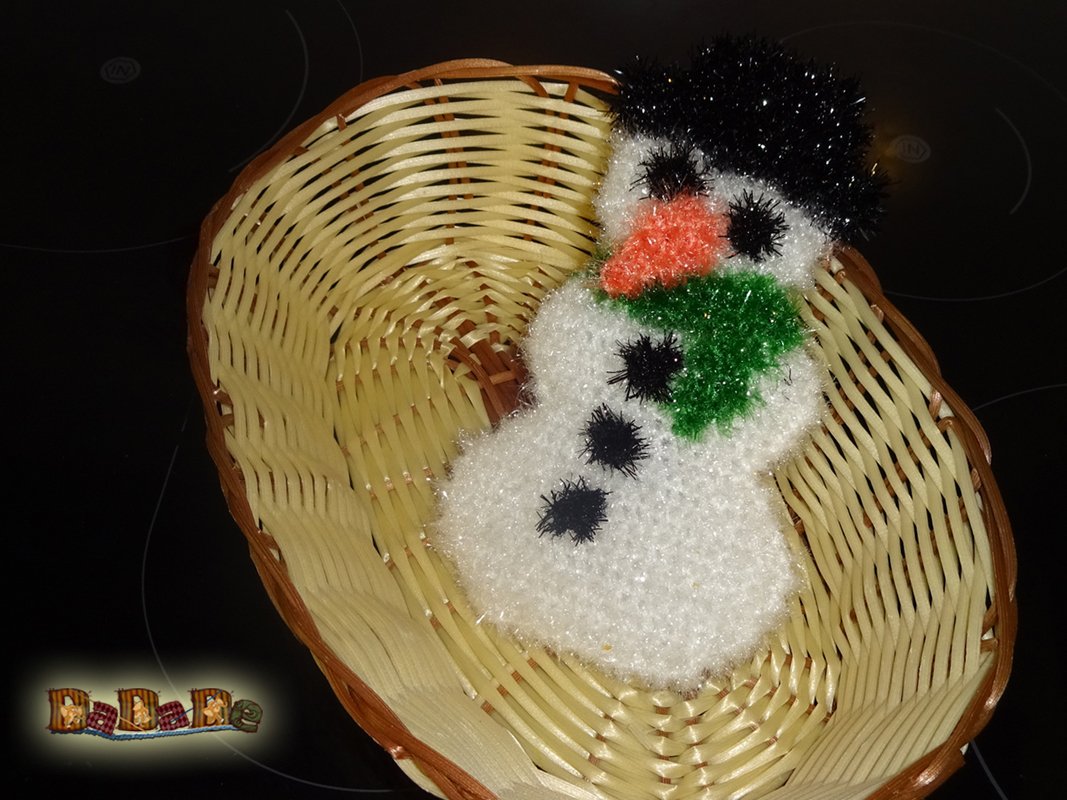 Gehäkelter Schneemann mit Hut und grünem Schal in einem Weidenkorb