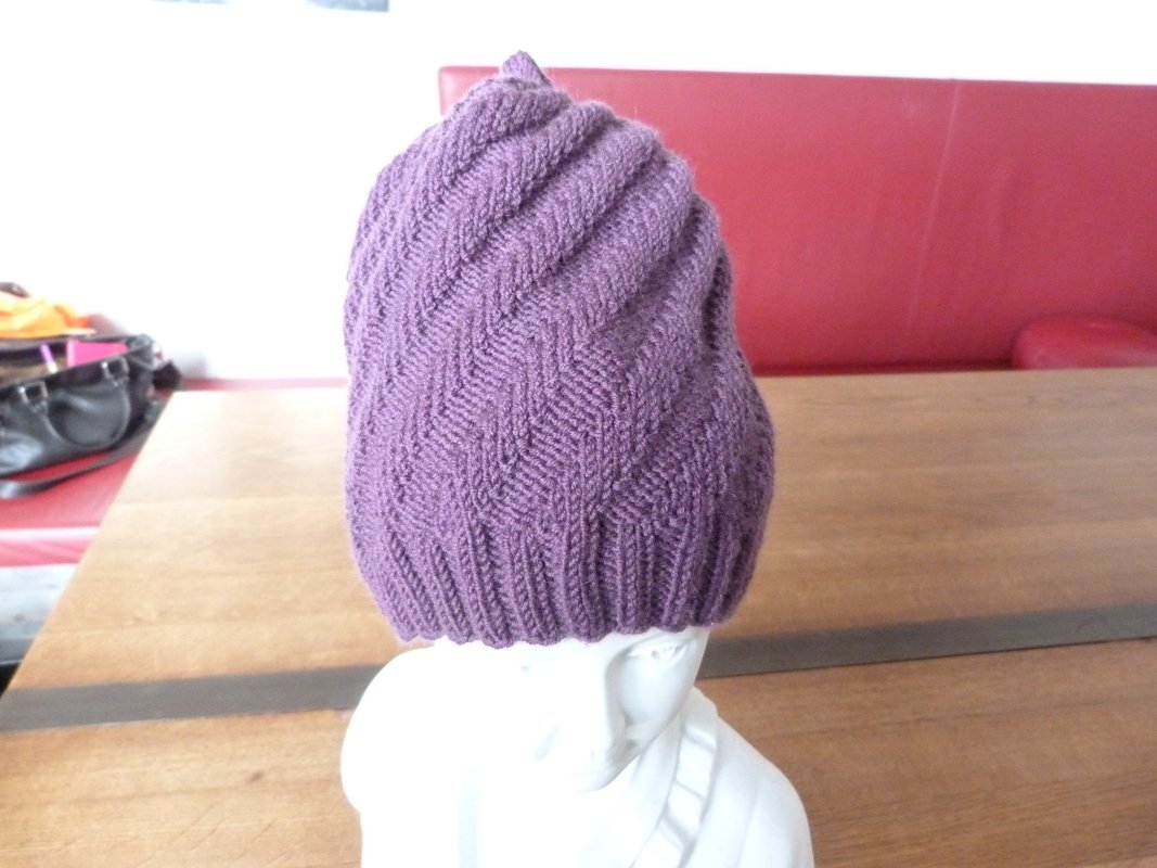 Lila gestrickte Mütze mit Fischgrätmuster auf weißem Mannequinkopf.