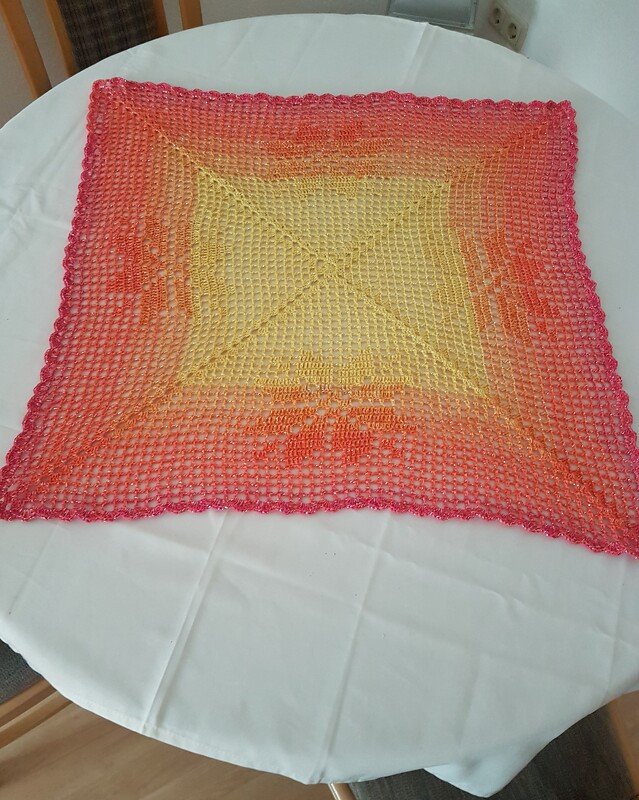 Quadratisches gehäkeltes Deckchen mit Farbverlauf (Gelb–Orange–Pink) auf weißer Tischdecke