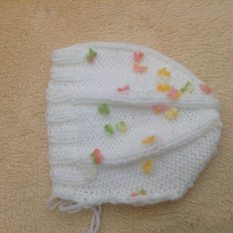 weiße gestrickte Babymütze mit Rippbündchen und bunten Knotenapplikationen