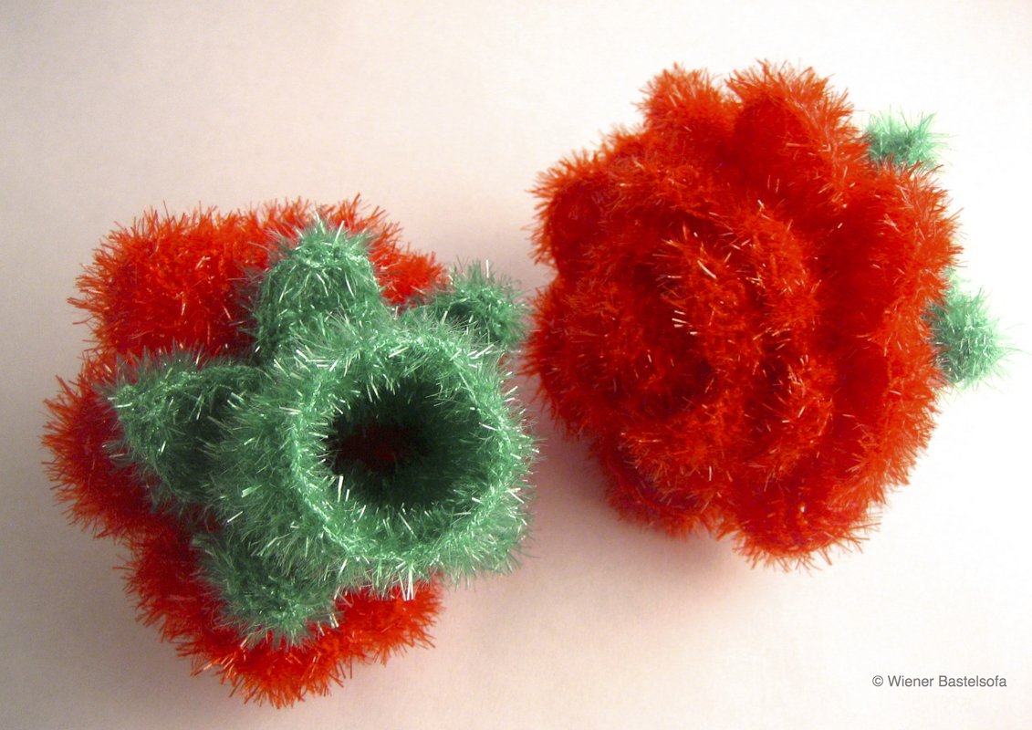 Zwei handgehäkelte, flauschige Objekte in Rot und Grün nebeneinander auf hellem Hintergrund.